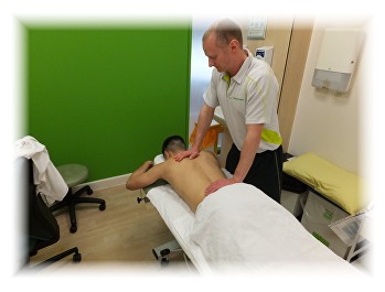 A therapist working on a client's back on a treatment couch in a small green-walled clinic room